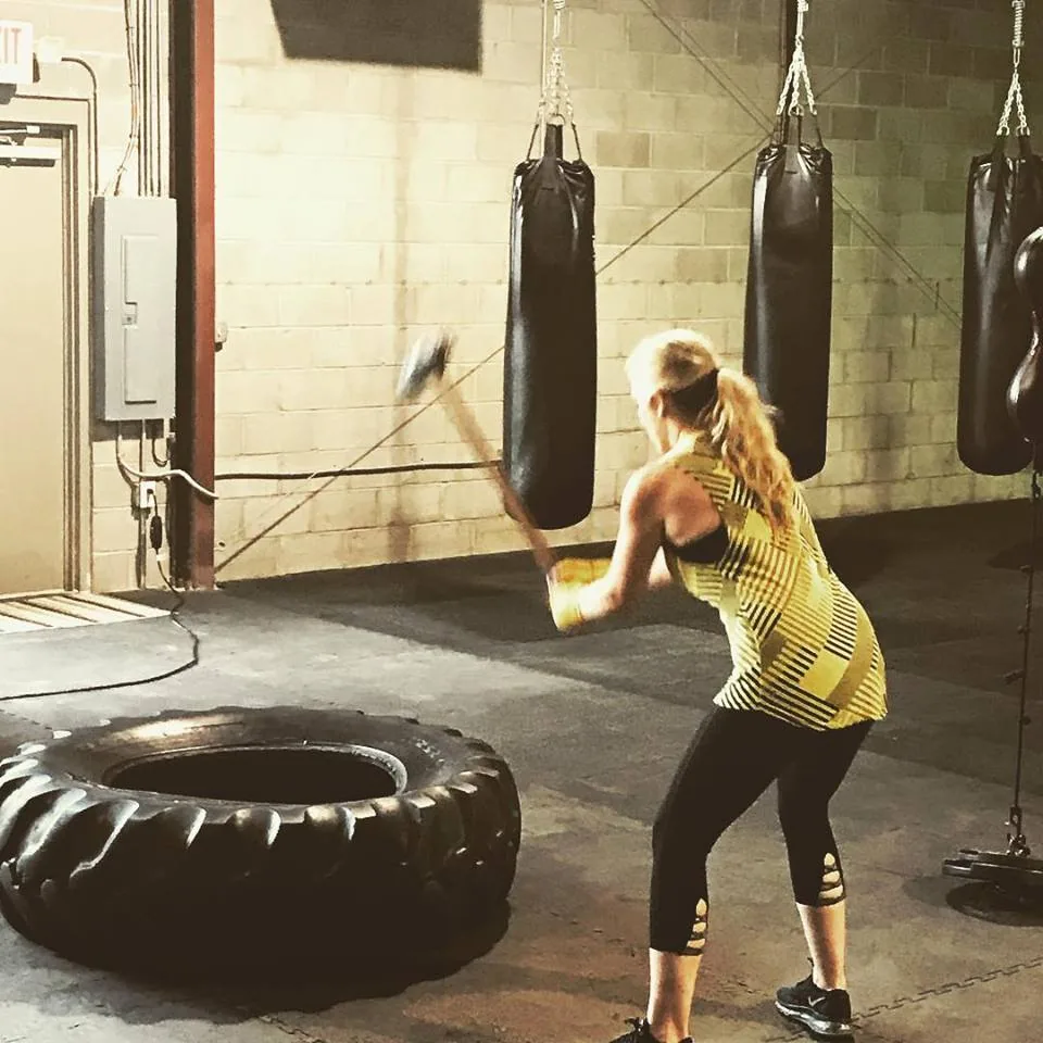A member swinging a sledgehammer into a tire beside the heavy bags.