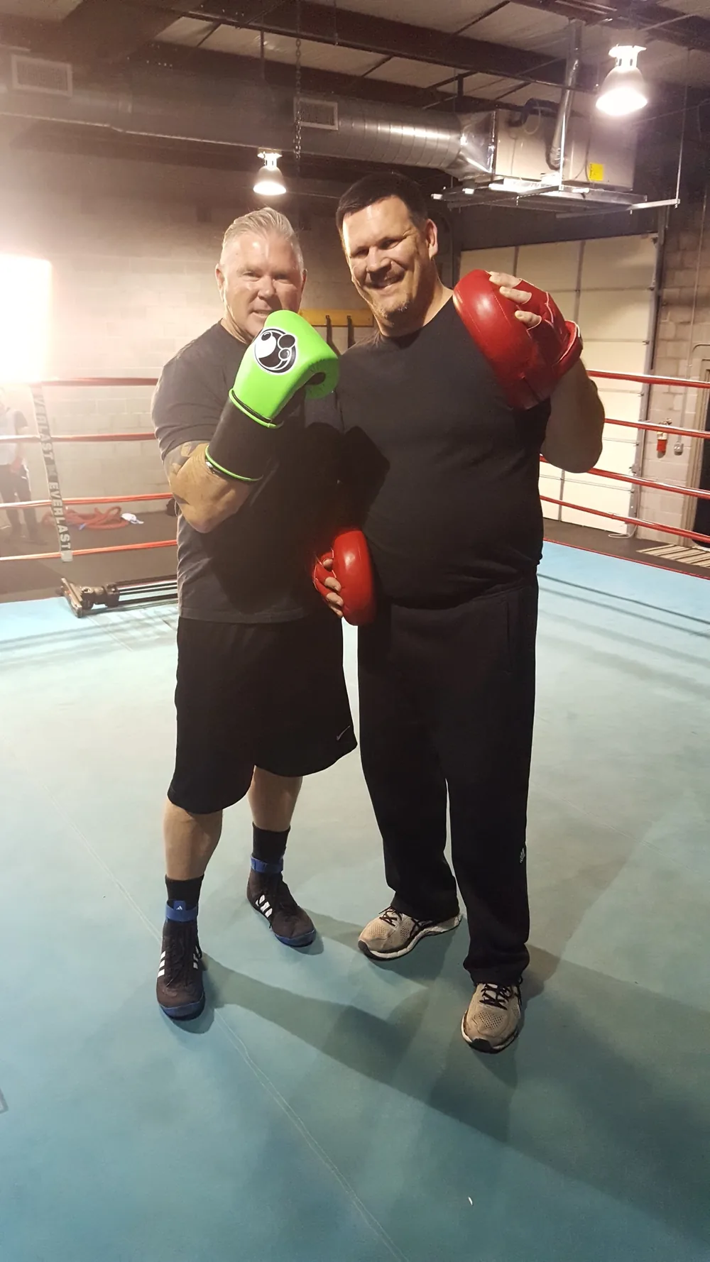 Two men in gloves and mitts standing together in the ring.
